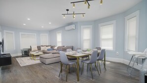 A spacious living room with a dining area, large windows, and a modern chandelier. - New England Traditional x Modern, 5 Bedrooms, Office, 8ppl (Quincy)