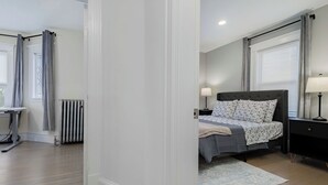 A bedroom with a bed, bedside tables, a radiator, and a window with curtains. - New England Traditional x Modern, 5 Bedrooms, Office, 8ppl (Quincy)
