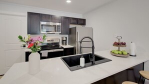 A modern kitchen with a central island, stainless steel appliances, and a decorative fruit and flower arrangement.