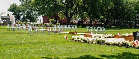 An outdoor seating area with white chairs arranged in rows, a flag, and a small building in the background.