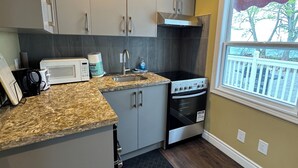Uma cozinha moderna com armários cinza, micro-ondas embutido, fogão e janela com vista para árvores.