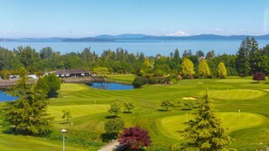 A golf course with a lake, trees, and a building in the background. - Modern Living Across from the Beach (Saanich North)