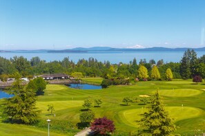 A golf course with a lake, trees, and a building in the background.