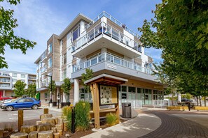 A modern multi-story building with a prominent address sign, outdoor seating, and a landscaped area with wooden posts and plants.