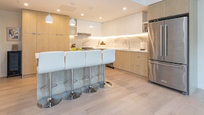 A modern kitchen with a stainless steel refrigerator, wooden cabinets, and a bar stool area. - Modern Living Across from the Beach (Saanich North)