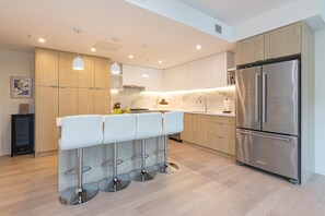 A modern kitchen with a stainless steel refrigerator, wooden cabinets, and a bar stool area.