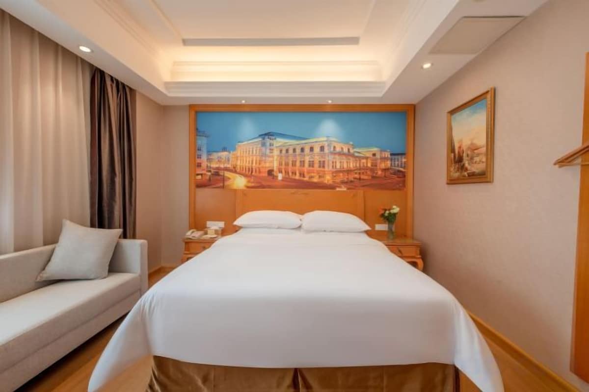 A hotel room with a bed, a sofa, a nightstand, and a painting on the wall.