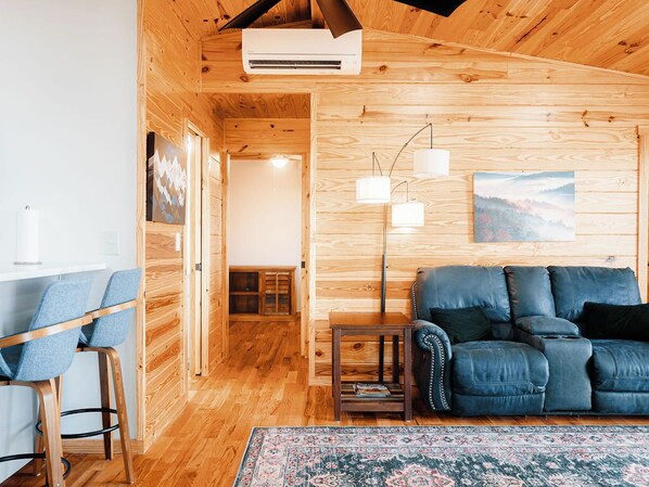 A cozy cabin interior with wooden walls, a blue leather sofa, a small side table, and a patterned rug. - Pops Cozy Cabin w/ an incredible valley view. Gas firepit, full kitchen and more (Fancy Gap)