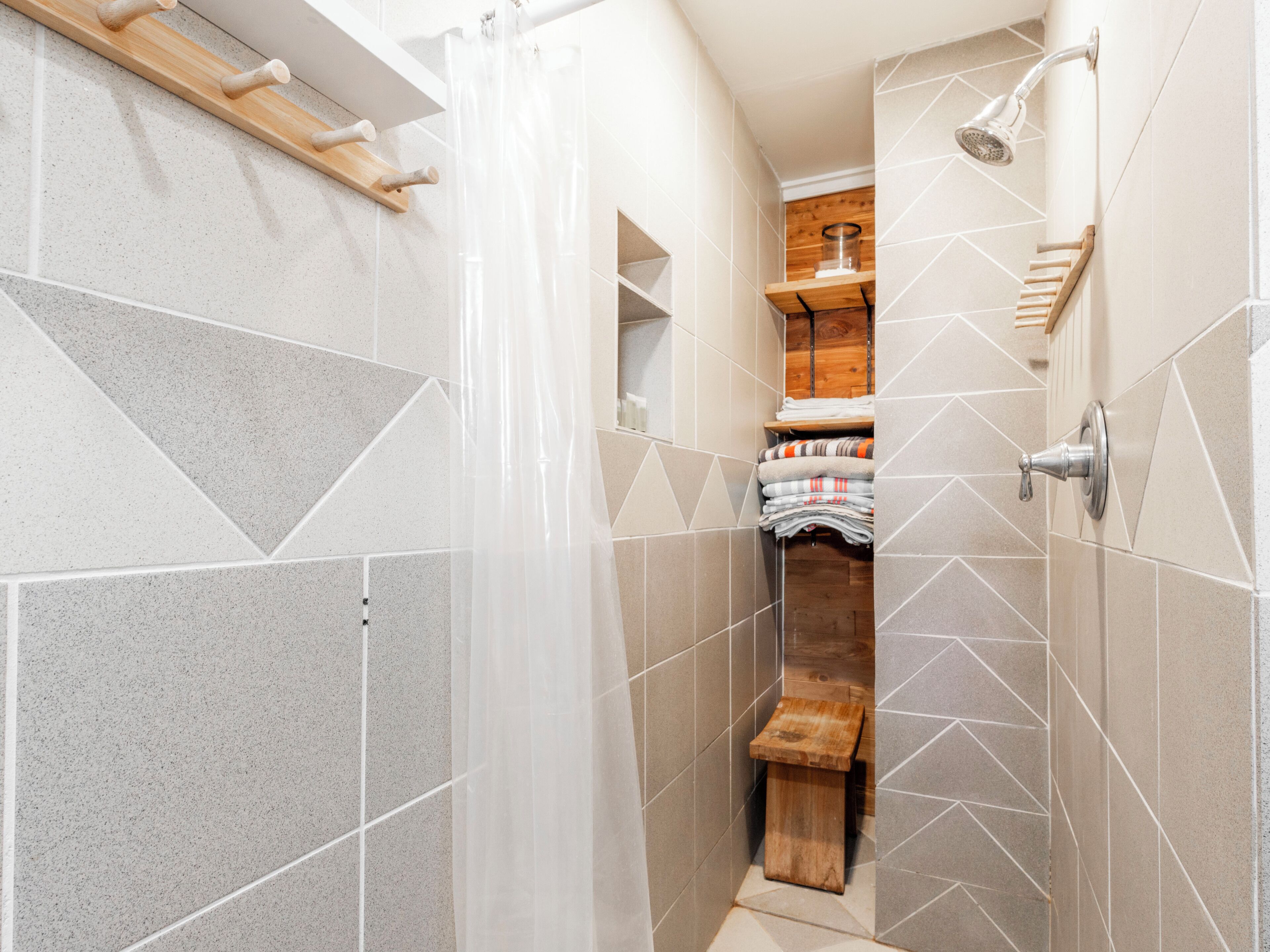 Een douche met een houten bankje, een glazen douchekop en een handdoekhouder.