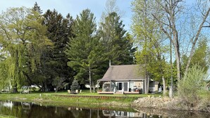 A lakeside property with a house, grassy areas, and trees. - Charming 3-bedroom riverside cottage in brilliant Tawas City (Tawas City)