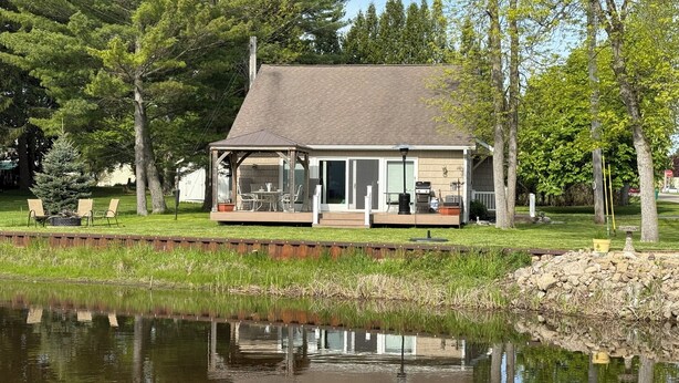 A house with a covered porch, a small deck, and a pond in front. - Charming 3-bedroom riverside cottage in brilliant Tawas City (Tawas City)