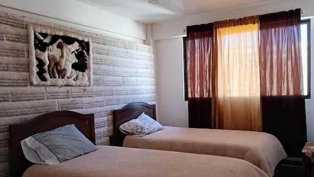 Une chambre avec deux lits, une tête de lit en bois, une œuvre d’art accrochée au mur et une fenêtre avec des rideaux.
