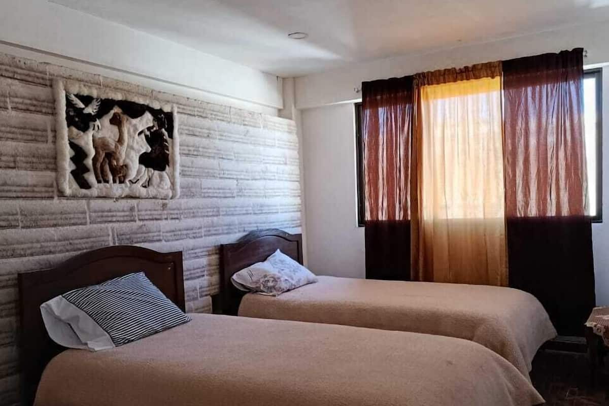 Ein Zimmer mit zwei Betten, einem Holz-Kopfteil, einem Wandbild und einem Fenster mit Vorhängen.