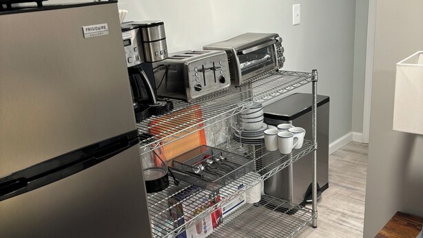 A kitchenette with a stainless steel refrigerator, a microwave, a toaster, and a coffee machine. There are shelves with kitchenware and a small table with a lamp. - Studio-close to Cleveland clinic With WiFi and AC in Cleveland Heights (Cleveland Heights)