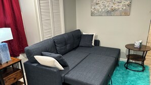 A grey sofa with a footrest, a small wooden side table, a teal furry rug, and a painting on the wall. - Studio-close to Cleveland clinic With WiFi and AC in Cleveland Heights (Cleveland Heights)