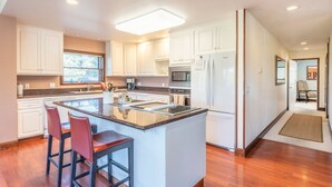 A modern kitchen with white cabinets, a central island with bar stools, a refrigerator, and a microwave. - Family Night's Rest | Game Room | Fort Bragg (Fort Bragg)