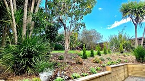 A garden with various plants and trees, a wooden bench, and a stone planter. - Guest Favorite 3BRM - New Reno with Parking & AC - CBD 12KMs & AP 17KMs  (Auckland)