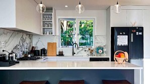 A modern kitchen with a large island, wooden stools, a black refrigerator, and a window with a view of greenery. - Guest Favorite 3BRM - New Reno with Parking & AC - CBD 12KMs & AP 17KMs  (Auckland)