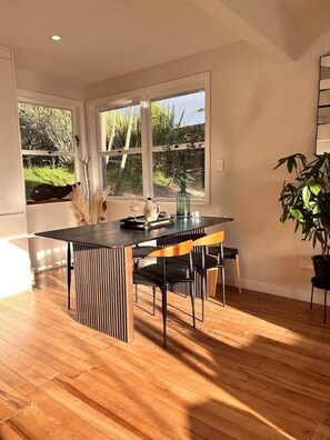 Ein zeitgemäßer Essbereich mit Holztisch, schwarzen Stühlen und Blick auf den Garten durch große Fenster.