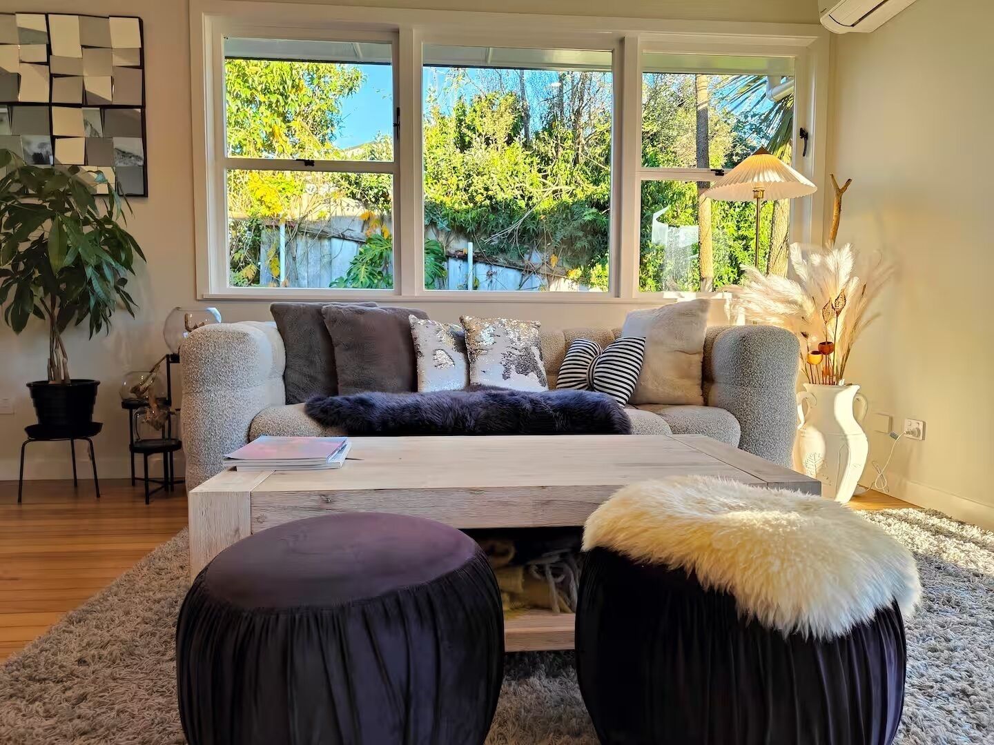 A cozy living room with a large window, a sofa, a coffee table, and a potted plant.