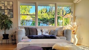 A cozy living room with a large window, a sofa, a coffee table, and a potted plant. - Guest Favorite 3BRM - New Reno with Parking & AC - CBD 12KMs & AP 17KMs  (Auckland)