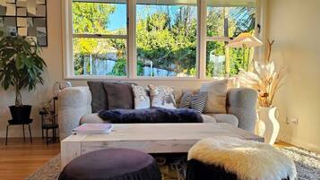 A cozy living room with a large window, a sofa, a coffee table, and a potted plant.