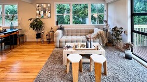 A spacious living room with a wooden floor, a beige sofa, a coffee table, and a dining area with a table and chairs. - Guest Favorite 3BRM - New Reno with Parking & AC - CBD 12KMs & AP 17KMs  (Auckland)