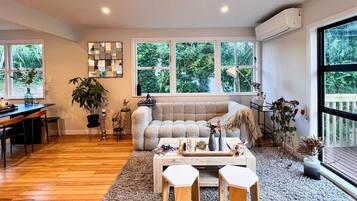 A spacious living room with a wooden floor, a beige sofa, a coffee table, and a dining area with a table and chairs.