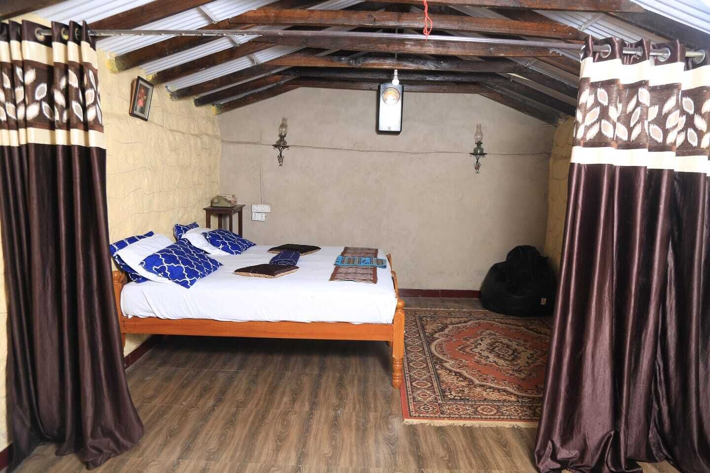 Ein gemütliches Schlafzimmer im Dachgeschoss mit einem hölzernen Bett, gemusterten Vorhängen, einem kleinen Teppich und einer Deckenleuchte.