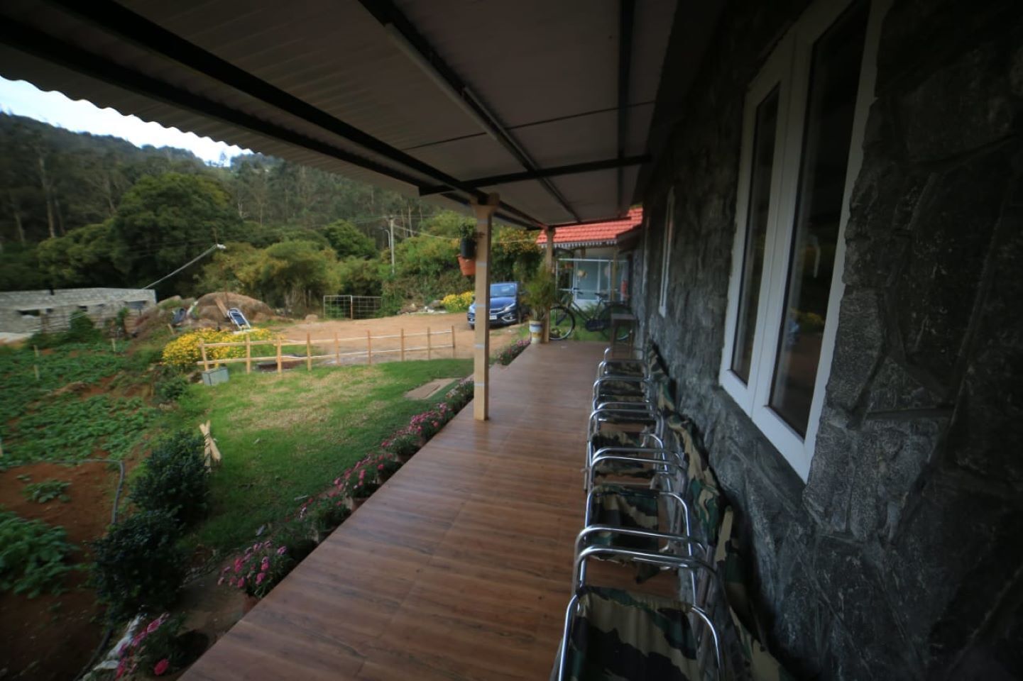 Un espacio al aire libre cubierto con cubierta de madera, paredes de piedra y vistas a un jardín y colinas.