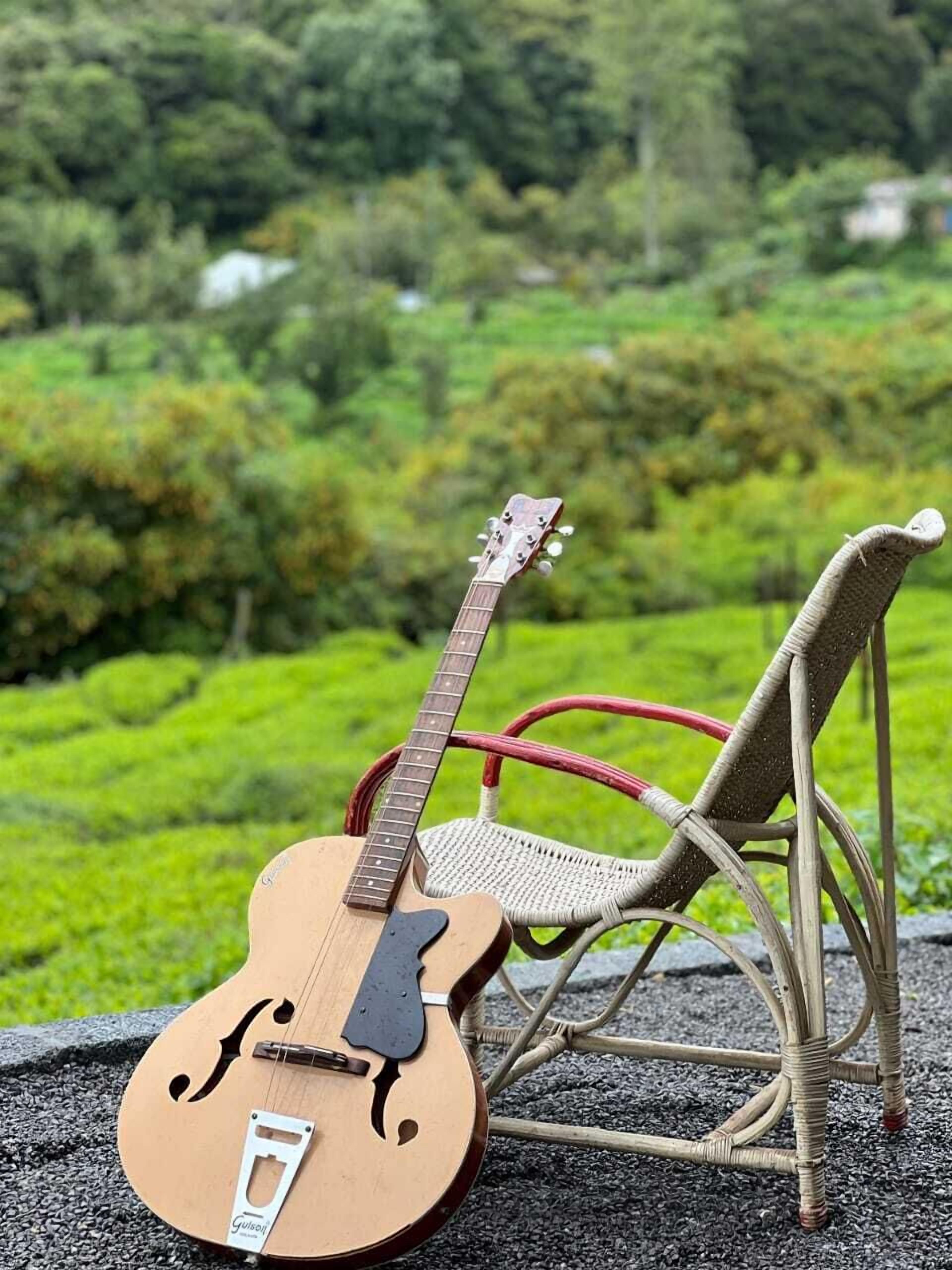 A guitar leaning against a wicker chair with a scenic view of a lush green landscape in the background.