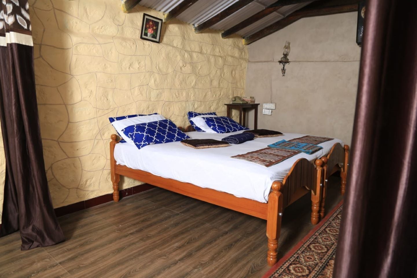 A bedroom with a wooden bed, a stone wall, a small bedside table, and a patterned rug.