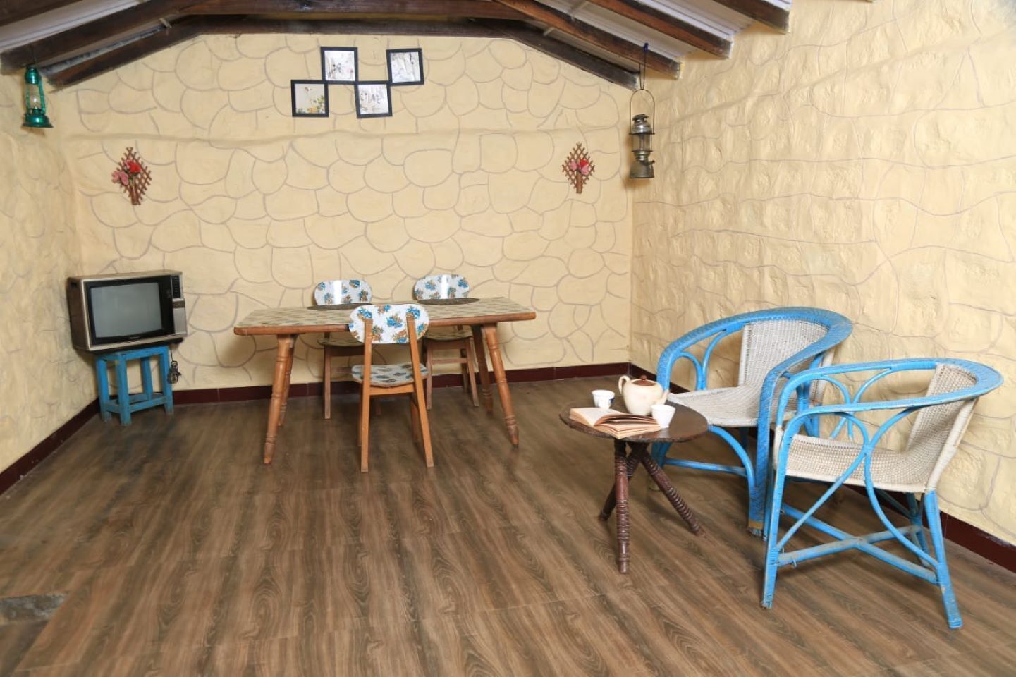 Una stanza accogliente con parete in pietra, pavimento in legno, un tavolo da pranzo con sedie, un piccolo televisore su un mobile e poltrone in vimini blu.