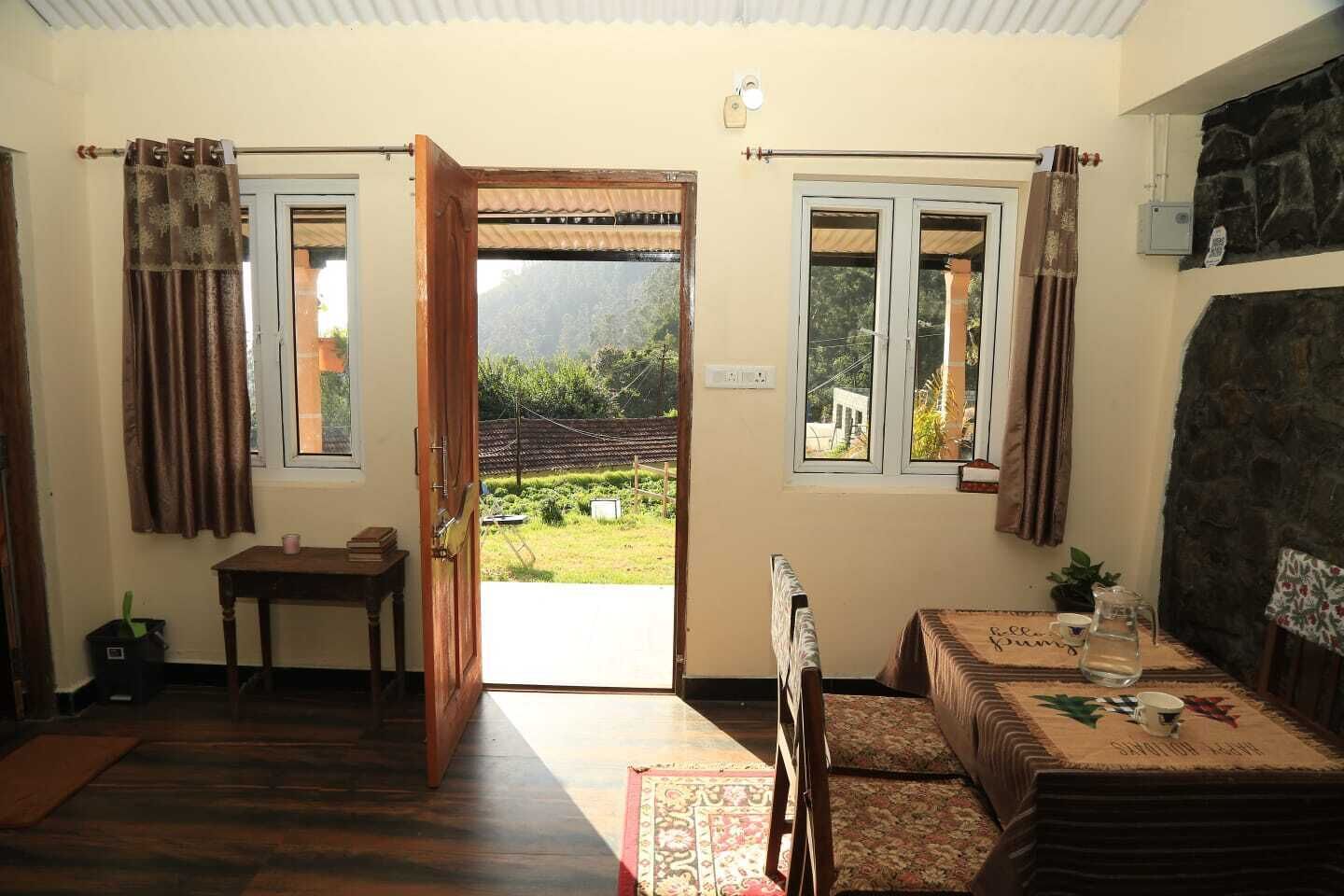 A room with a wooden floor, a table with a tablecloth, a radiator, and a view of a garden through an open door.