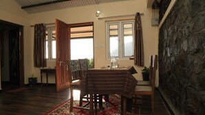 Ein Zimmer mit Esstisch, Stühlen, Teppich, einem Fenster mit Vorhängen und einer Steinwand.