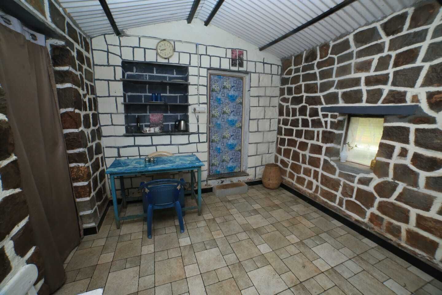 A small room with a tiled floor, a blue table with chairs, a clock on the wall, and a door with a decorative window.