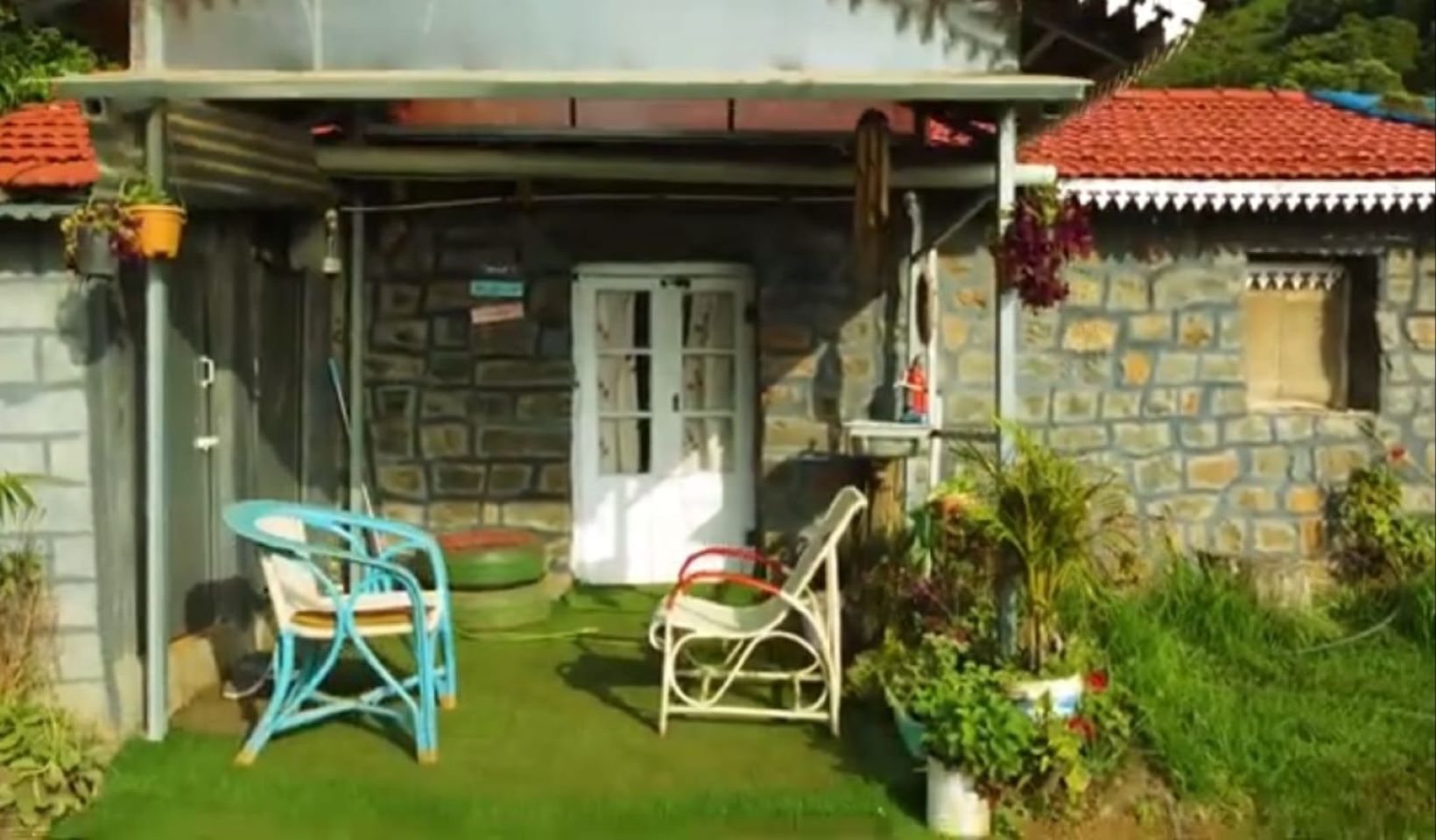 Un edificio in pietra con tetto in tegole rosse, un portone e un piccolo portico con due sedie e un tavolo.