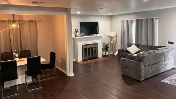 Un salon moderne avec un canapé gris, un coin repas comprenant une table et des chaises, une cheminée et un téléviseur fixé au-dessus.