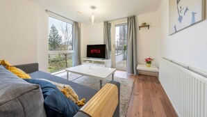 Una sala de estar moderna con un sofá, una mesa de centro, un televisor sobre un mueble bajo y un balcón con vistas.