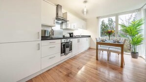 Una cocina moderna con armarios blancos, encimera negra y una mesa de comedor de madera para cuatro comensales.