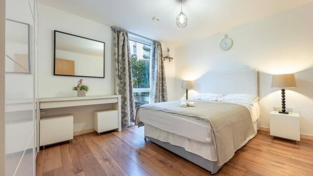 Un dormitorio con cama, mesitas de noche, escritorio, espejo y ventana con cortinas.