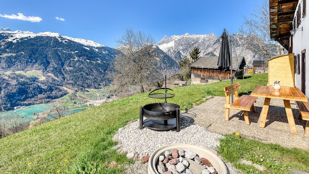 A patio with a grill, wooden table, and chairs overlooking a mountainous landscape. - Chalet Zimbablick in Bartholom Berg (Bartholomaeberg)