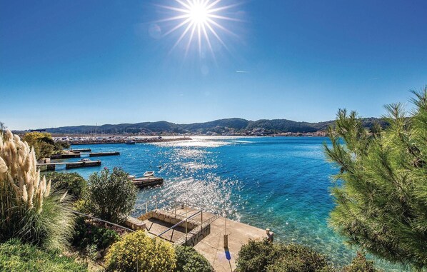A coastal marina with boats docked, clear blue water, and a mountainous backdrop.