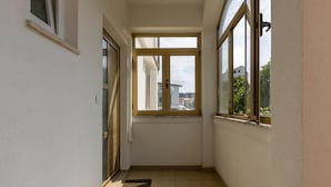 A narrow corridor with a tiled floor, a door, and a window with a view of buildings and greenery outside.
