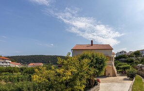 A residential building with a red-tiled roof, surrounded by lush greenery and a clear sky.