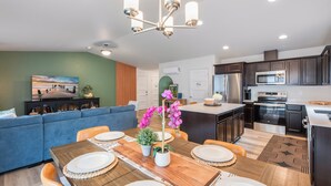 Una cocina moderna con armarios oscuros, electrodomésticos de acero inoxidable y una mesa de comedor de madera para cuatro comensales.