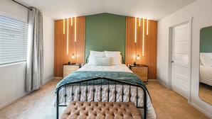 Un dormitorio con cama, mesitas de noche, un banco, un armario y una ventana con cortinas.