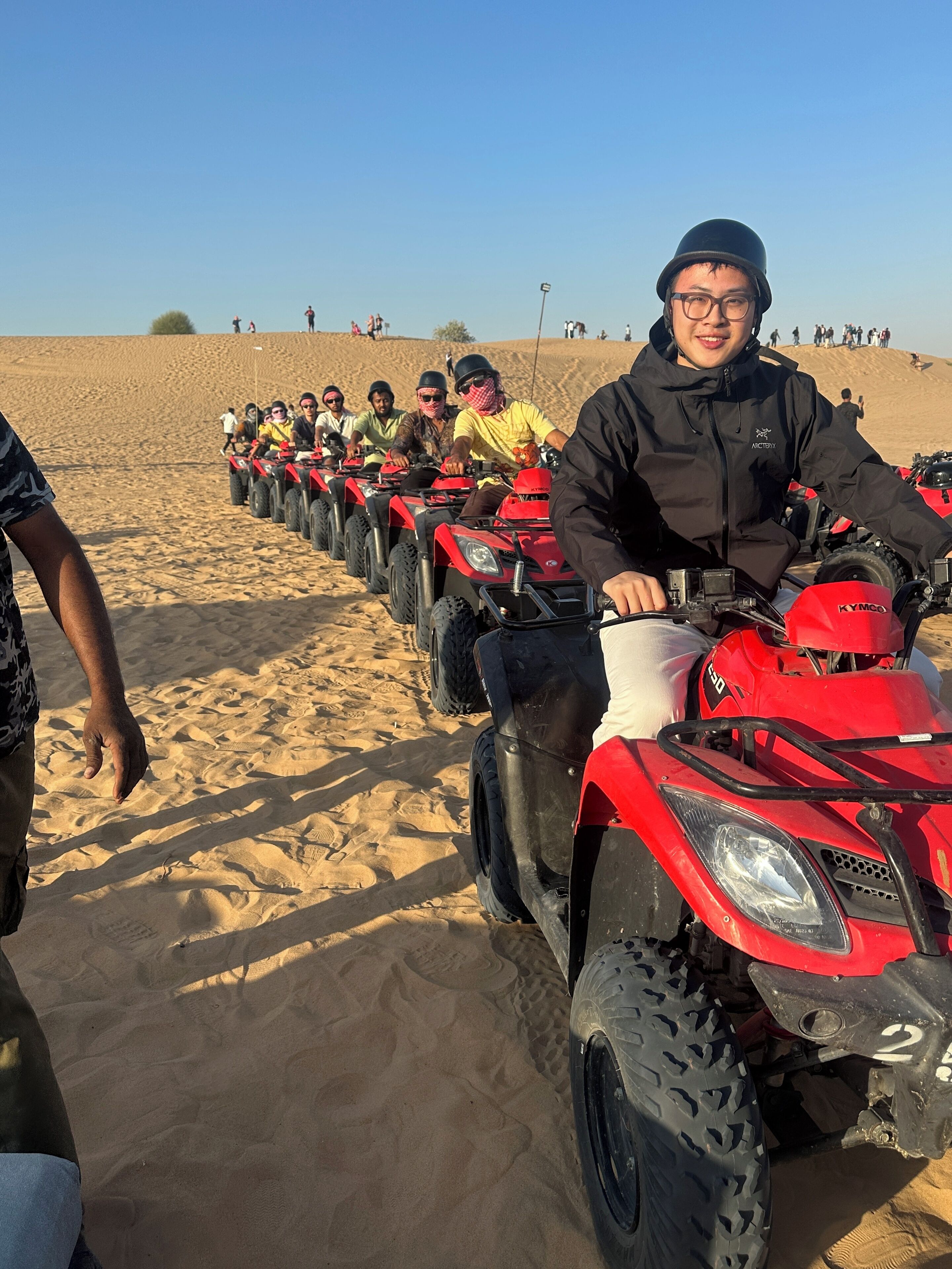 A row of red ATVs on a sandy beach with people riding them.