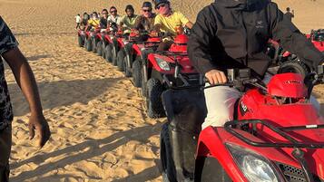A row of red ATVs on a sandy beach with people riding them.