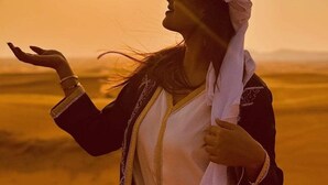 Une personne vêtue d’un costume traditionnel, avec un paysage désertique en arrière-plan.
